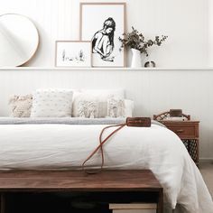 a bed with white sheets and pillows in a bedroom next to a dresser, mirror and pictures on the wall