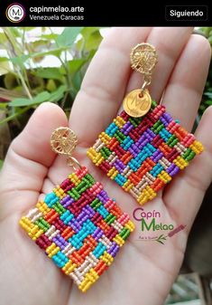 a person is holding some colorful beaded earrings in their hand and it has a gold disc on the end