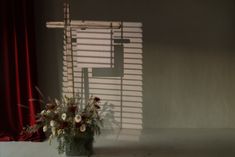 a vase filled with flowers sitting in front of a window covered in red curtains and blinds