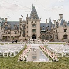 an outdoor ceremony setup with white chairs and pink flowers in front of a large building