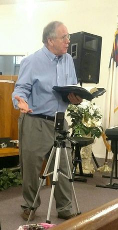 an older man standing in front of a camera holding a clipboard and looking at something on a tripod