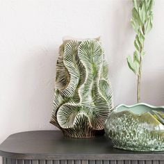 two green vases sitting on top of a wooden table next to a white wall