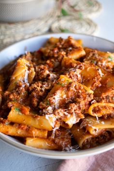 a white bowl filled with pasta covered in meat and sauce on top of a table