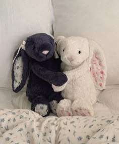 two stuffed animals sitting next to each other on a bed