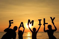 three people holding up letters that spell out the word family in front of an ocean at sunset