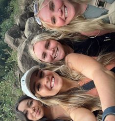 three women standing next to each other in front of some rocks and trees with their arms around one another