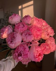 a bouquet of pink peonies sitting on top of a wooden table next to a window