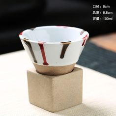 a white and brown bowl sitting on top of a wooden block next to a table