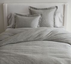 an unmade bed with grey linens and pillows