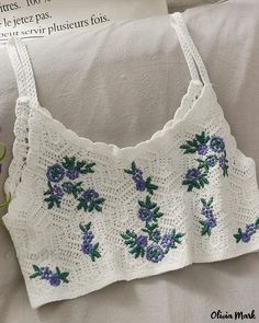 a crocheted top with flowers on it sitting on a white pillow next to a plant