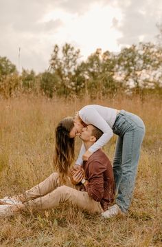 a man and woman kissing while sitting in the grass