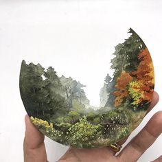 a person holding up a paper cutout with trees in the background and foliage around it