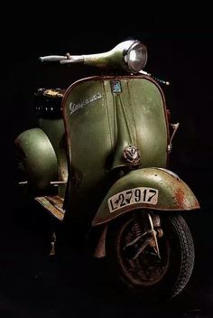 an old green scooter is parked on the dark ground in front of a black background