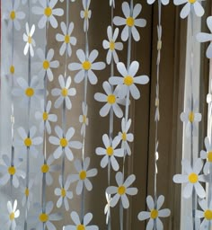 some white and yellow flowers are hanging from the window sill in front of a curtain