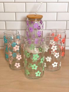 four glasses with flowers painted on them sitting next to each other in front of a white brick wall