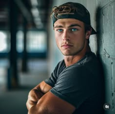 a young man leaning against a wall with his arms crossed and looking at the camera