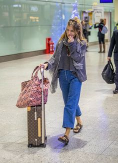 a woman is walking through an airport with her luggage and talking on the cell phone