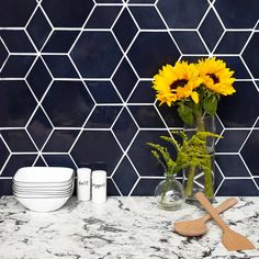 sunflowers in a vase on a marble countertop with white plates and utensils