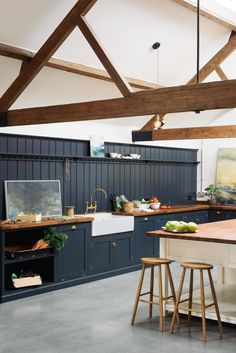 an open kitchen with blue cabinets and wood beams on the ceiling, along with wooden stools