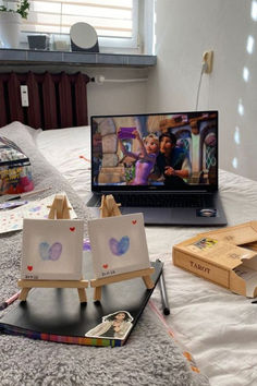 an open laptop computer sitting on top of a bed next to two small easels