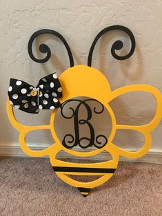 a yellow and black bee with polka dot bow on it's head sitting in front of a wall