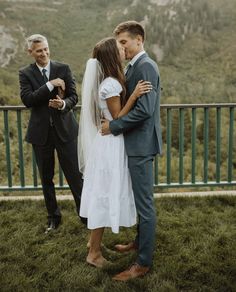 two men and a woman are standing in the grass with their arms around each other