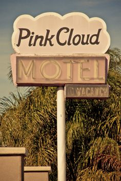 the pink cloud motel sign is in front of some palm trees and bushes, against a blue sky