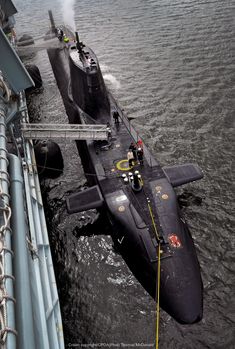 a black submarine floating on top of the ocean next to a tug boat in the water