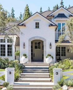 a white house with steps leading up to the front door and entry way, surrounded by greenery