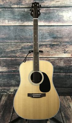 an acoustic guitar sitting on top of a wooden stand in front of a wood wall