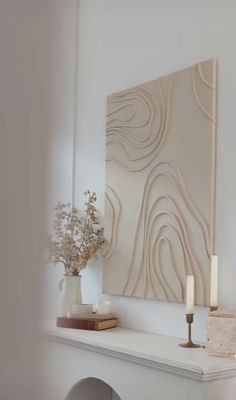 a white mantle with candles and vases on it in front of a wall art piece