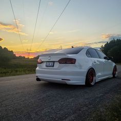 the white car is parked on the side of the road near power lines at sunset