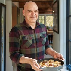 a man holding a pan full of food in his hands and smiling at the camera