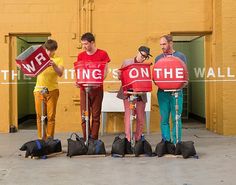 three people standing in front of a building holding signs and wearing red vests with the words, waiting is on the wall