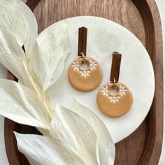 two brown and white earrings sitting on top of a plate next to a leafy plant