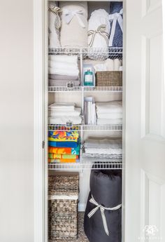 an organized closet with white linens and other items in baskets on the bottom shelf