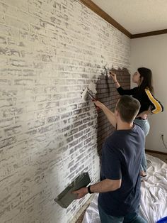 two people are painting a brick wall with paint rollers in the process of remodeling