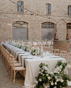 the tables are set with white flowers and greenery for an elegant wedding reception in front of a brick building