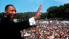 a man giving a speech in front of a large crowd with his hands up to the sky