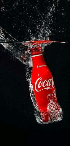 a coca - cola bottle floating in the water with its splashing on it's side