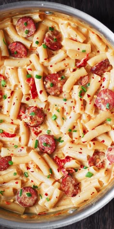 a pan filled with pasta and sausages on top of a wooden table next to utensils