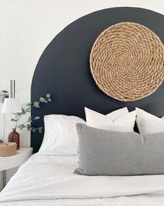 a bed with white linens and pillows in a small room next to a round wicker wall decoration