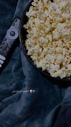 a black bowl filled with popcorn next to a remote control on a blue cloth covered surface