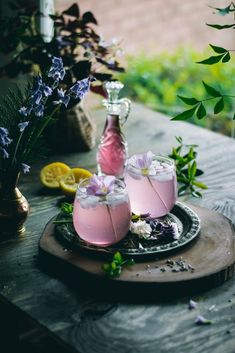 two glasses filled with pink liquid sitting on top of a wooden table next to flowers