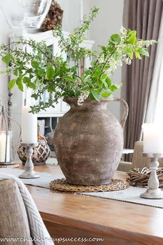 a vase filled with greenery sitting on top of a wooden table next to candles