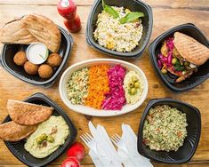 a table topped with black plastic containers filled with different types of food and utensils