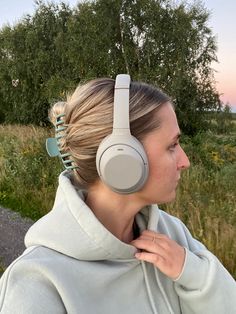 a woman wearing headphones standing in front of some grass and trees, with her back to the camera