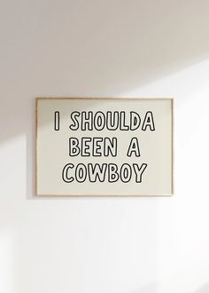 a sign that says i should be a cowboy hanging on the wall in a room