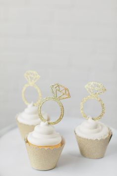 three cupcakes with gold glitter rings on top and white frosting in the middle