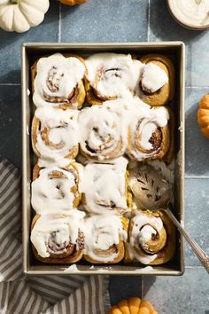 a pan filled with cinnamon buns covered in icing next to mini pumpkins